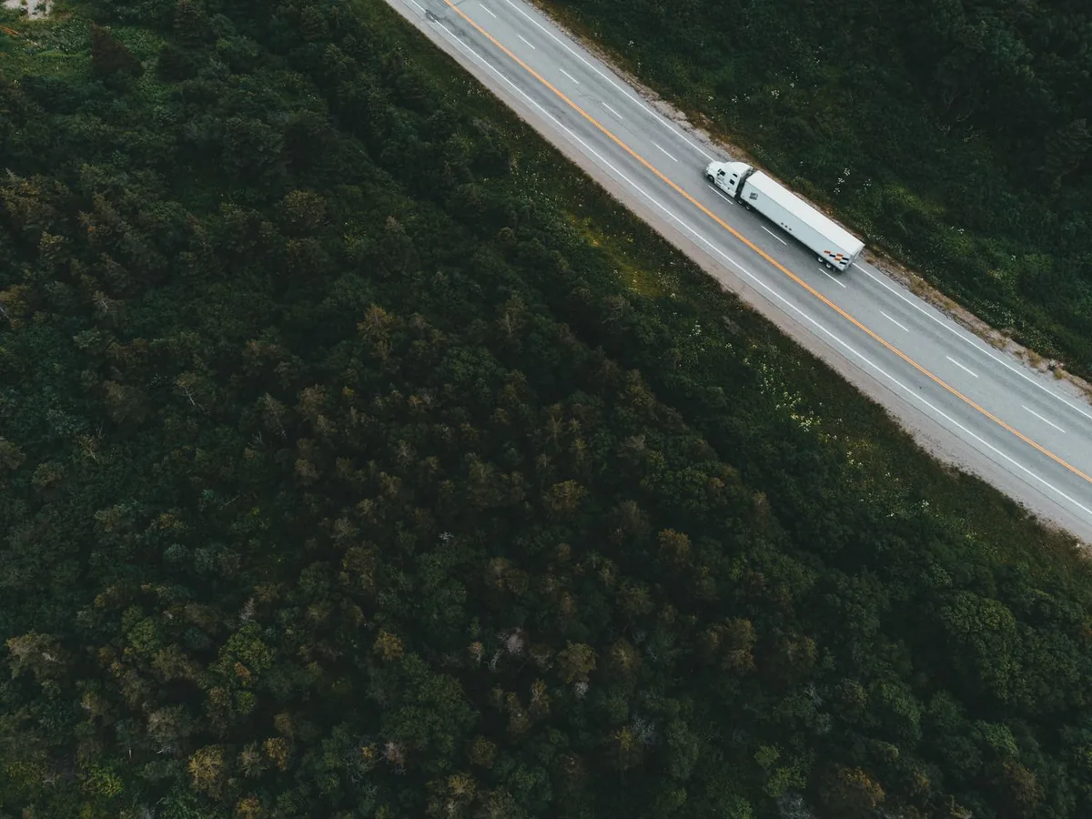 White semi-trailer truck traveling along a forested highway